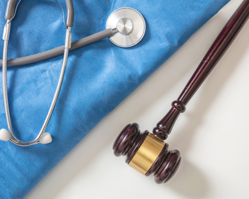 A wooden gavel rests beside a stethoscope placed on a folded blue medical gown. The image supports a legal blog explaining why expert witnesses are essential in Massachusetts medical malpractice cases and how their testimony helps prove negligence and establish the standard of care.
